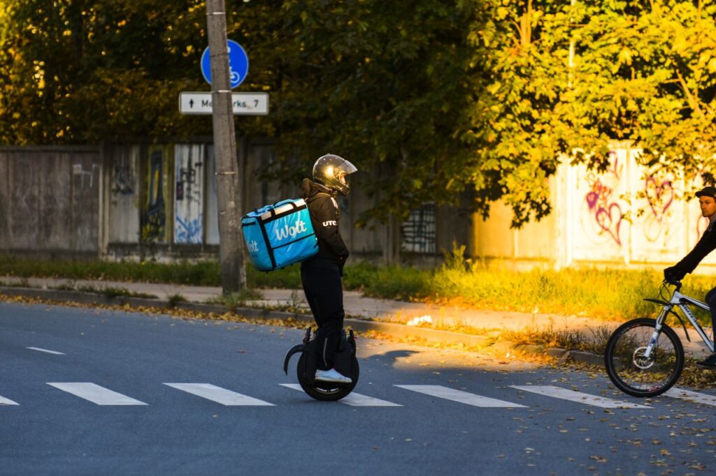 Delivery rider on electric unicycle crossing Riga street in evening light.