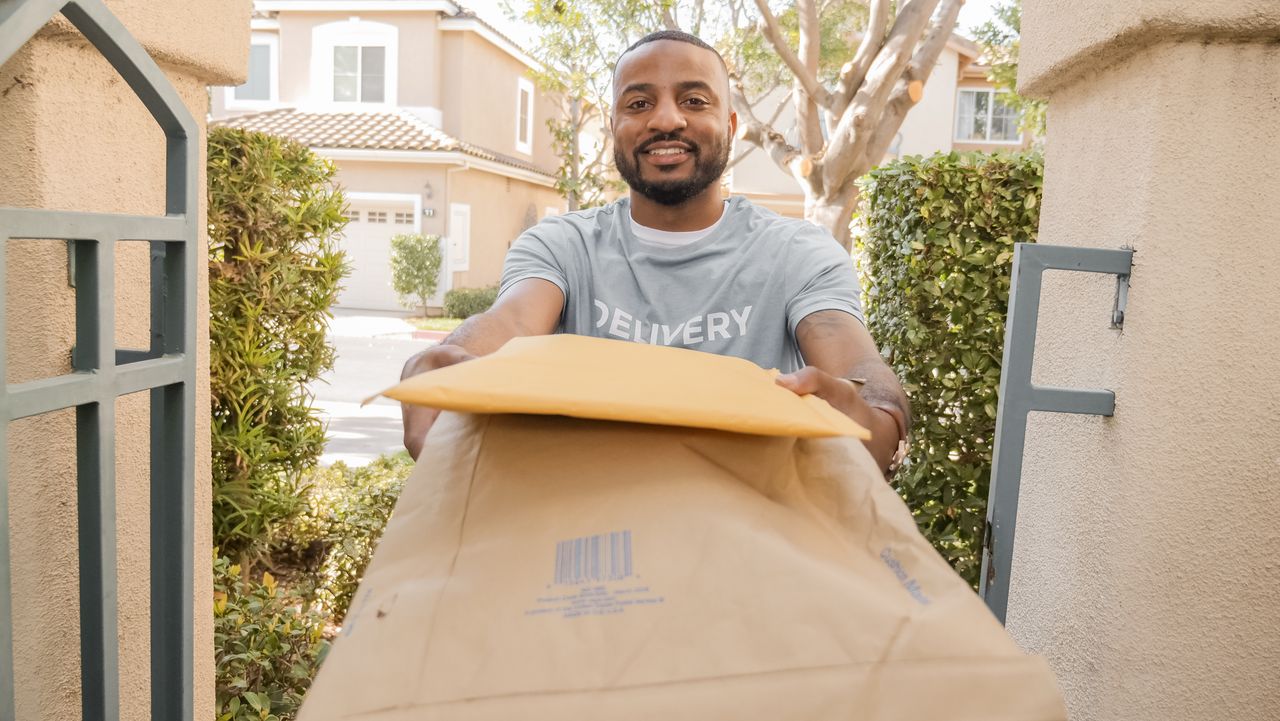 African American delivery man smiling while handing over parcels outdoors.